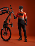 A-Dura ASTARS Långärmad Tröja 2.0 i orange-svart gradient med logotyp, visas med mountainbike-utrustning.