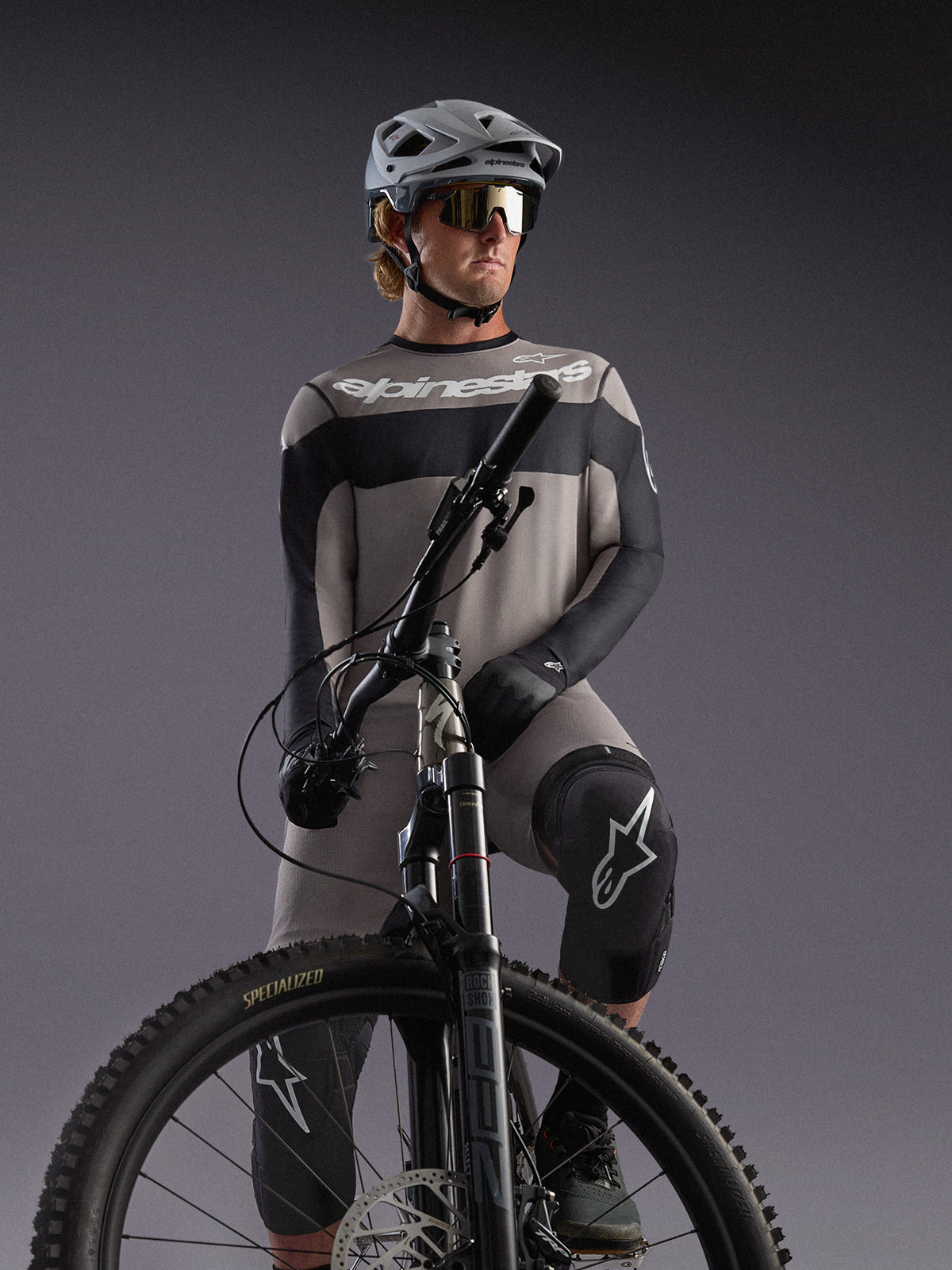 Grå Alpinestars A-Dura Race långärmad tröja på en MTB-cyklist, med svarta detaljer och professionell utrustning.