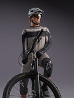 Grå Alpinestars A-Dura Race långärmad tröja på en MTB-cyklist, med svarta detaljer och professionell utrustning.