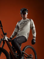 A-Dura Ride långärmad tröja i Sand Camo med Alpinestars logotyp, buren av en MTB-cyklist på en mountainbike.