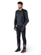 Alpinestars Missile V3 läderjacka, svart, bärs av en förare med svarta byxor och svart-röda racinghandskar och stövlar, med perforerade läderpaneler och elegant monokrom logotyp, professionell racing-estetik