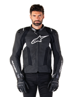 Alpinestars Missile V3 läderjacka, svart med vita logotyper, bärs av en modell med svarta körhandskar, premium motorcykelracingjacka i läder med perforerade ventilationspaneler och prestandafunktioner