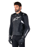 Alpinestars Missile V3 skinnjacka, svart och vit, bärs av en man med svarta körhandskar, med en framträdande vit Alpinestars-logotyp på bröstet, externa axelsliders och perforerade paneler för en racinginspirerad look.