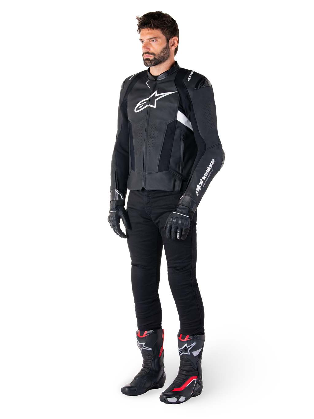 Manlig förare som bär Alpinestars Missile V3 skinnjacka i svart och vitt, med en vit bröstlogotyp och perforerade läderpaneler, matchad med svarta körbyxor, svarta handskar och svarta och röda racingstövlar för en komplett sportig look.
