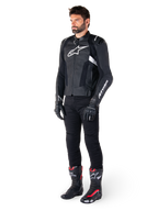 Manlig förare som bär Alpinestars Missile V3 skinnjacka i svart och vitt, med en vit bröstlogotyp och perforerade läderpaneler, matchad med svarta körbyxor, svarta handskar och svarta och röda racingstövlar för en komplett sportig look.