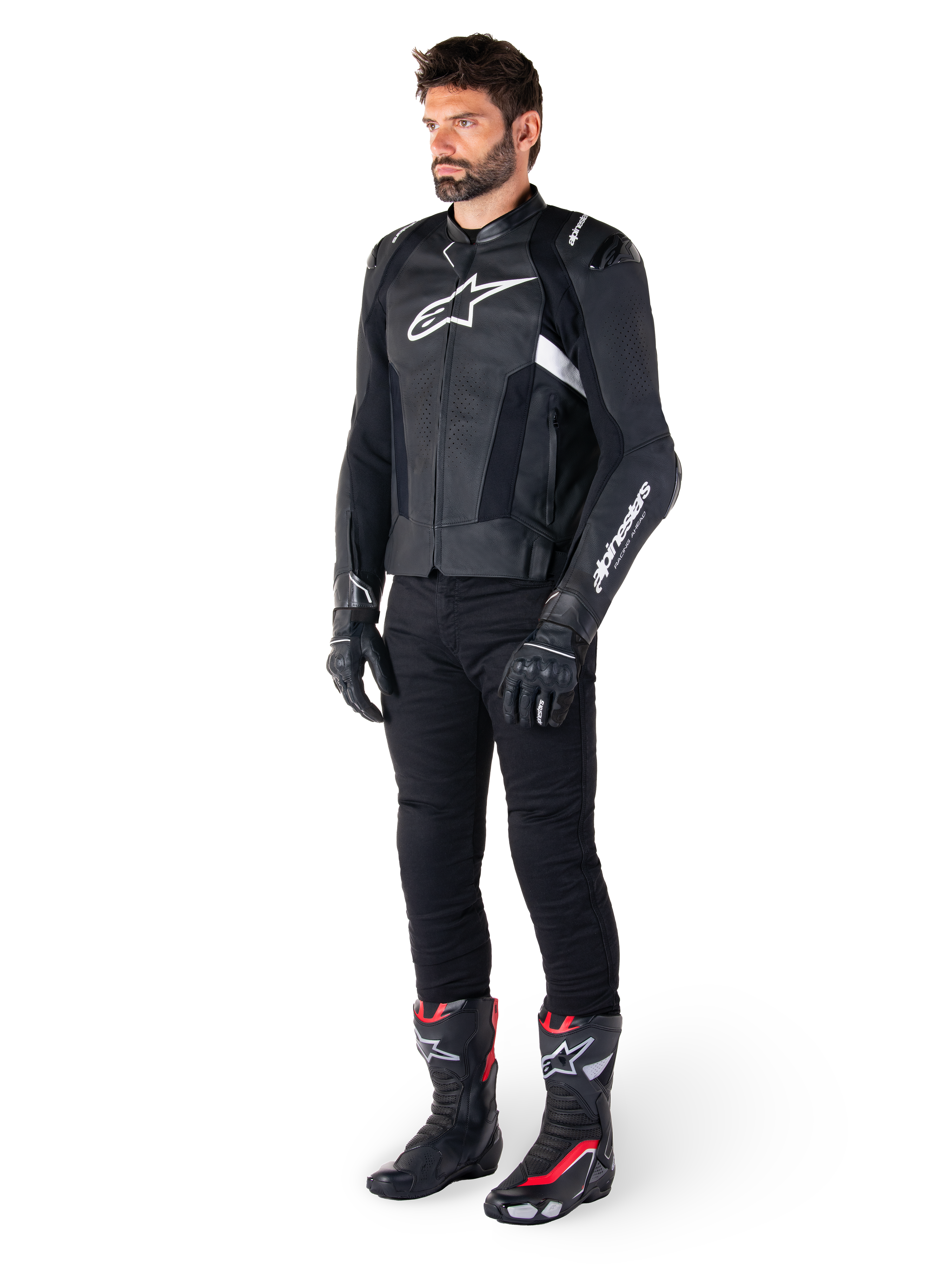 Manlig förare som bär Alpinestars Missile V3 skinnjacka i svart och vitt, med en vit bröstlogotyp och perforerade läderpaneler, matchad med svarta körbyxor, svarta handskar och svarta och röda racingstövlar för en komplett sportig look.