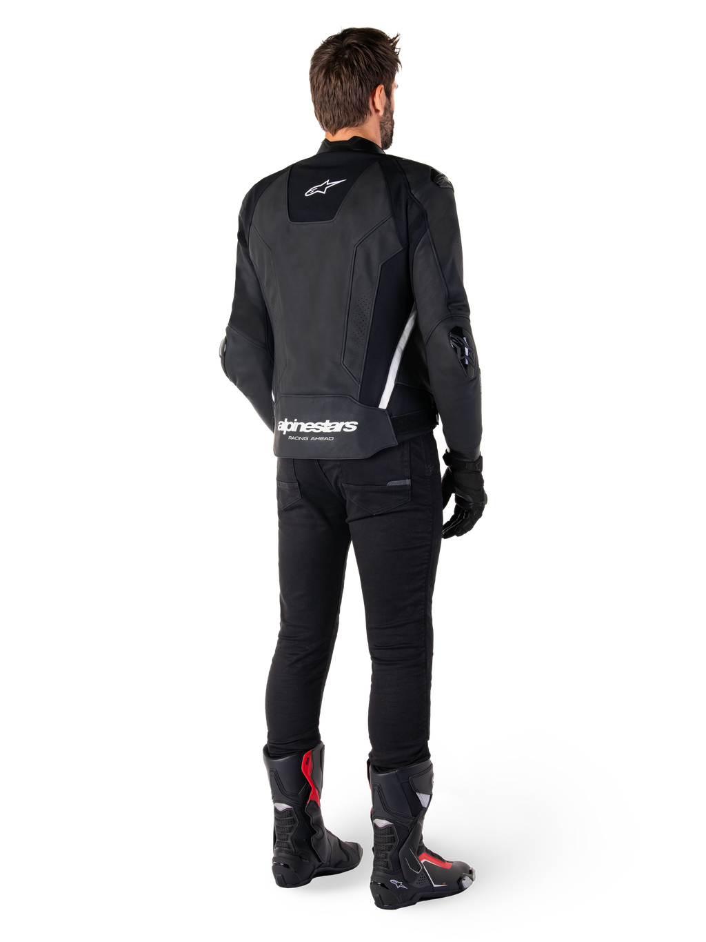 Alpinestars Missile V3 Skinnjacka, svart och vit, vy bakifrån på förare, med framträdande vit Alpinestars-logotyp på nedre delen av ryggen och en liten logotyp på övre delen, bärs med svarta byxor och racingstövlar, premium skinnkonstruktion för motorcykelracing