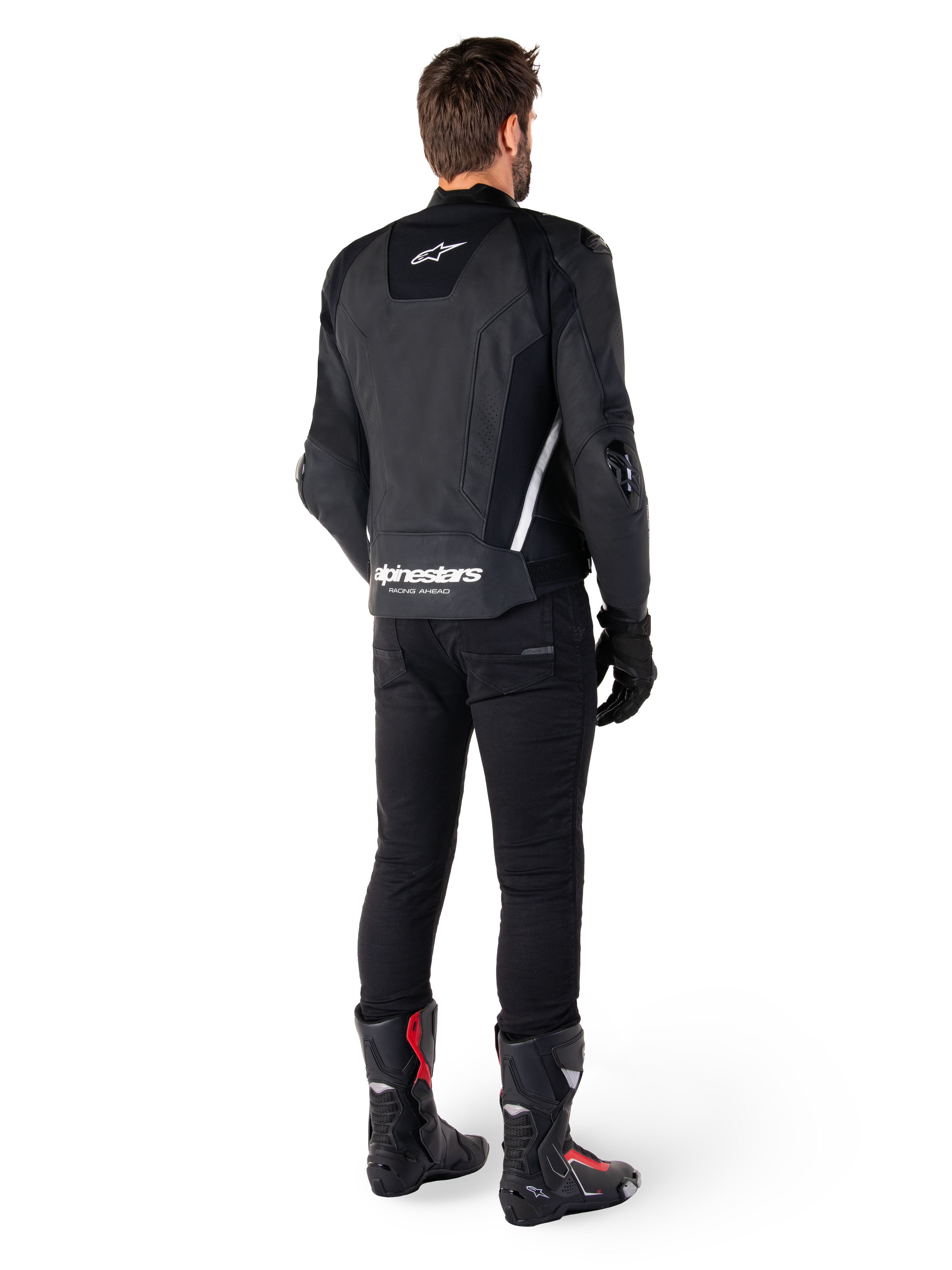 Alpinestars Missile V3 Skinnjacka, svart och vit, vy bakifrån på förare, med framträdande vit Alpinestars-logotyp på nedre delen av ryggen och en liten logotyp på övre delen, bärs med svarta byxor och racingstövlar, premium skinnkonstruktion för motorcykelracing