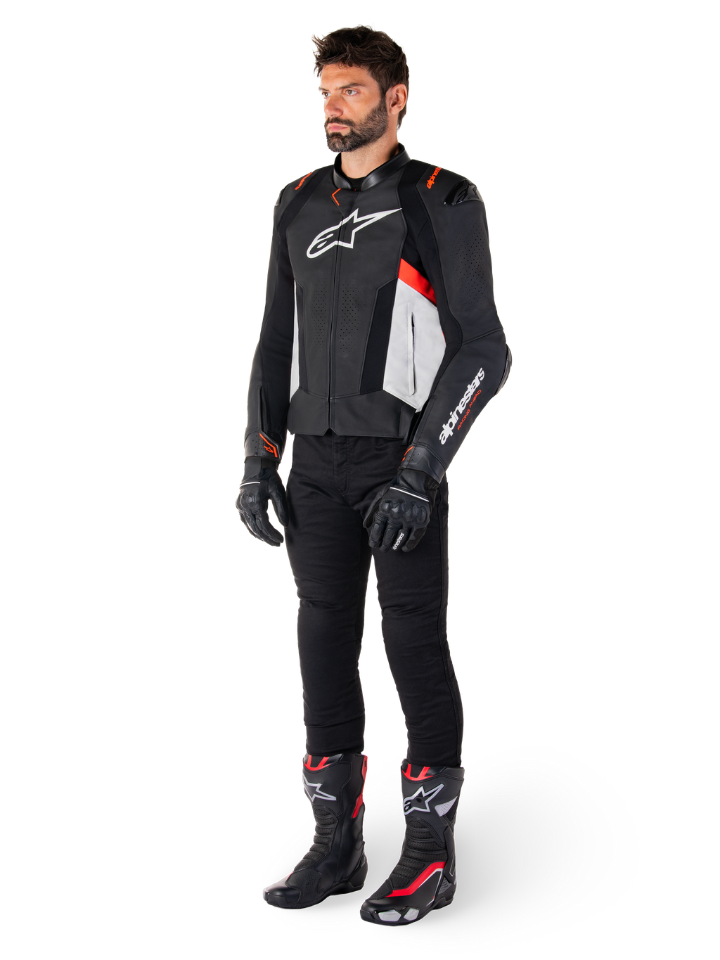Manlig modell iklädd Alpinestars Missile V3 läderjacka i svart, vitt och röd fluo, kombinerad med svarta motorcykelbyxor, handskar och stövlar, tillverkad i premium nötläder med framträdande Alpinestars-logotyper, professionell racing-sportestetik