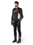 Manlig modell iklädd Alpinestars Missile V3 läderjacka i svart, vitt och röd fluo, kombinerad med svarta motorcykelbyxor, handskar och stövlar, tillverkad i premium nötläder med framträdande Alpinestars-logotyper, professionell racing-sportestetik