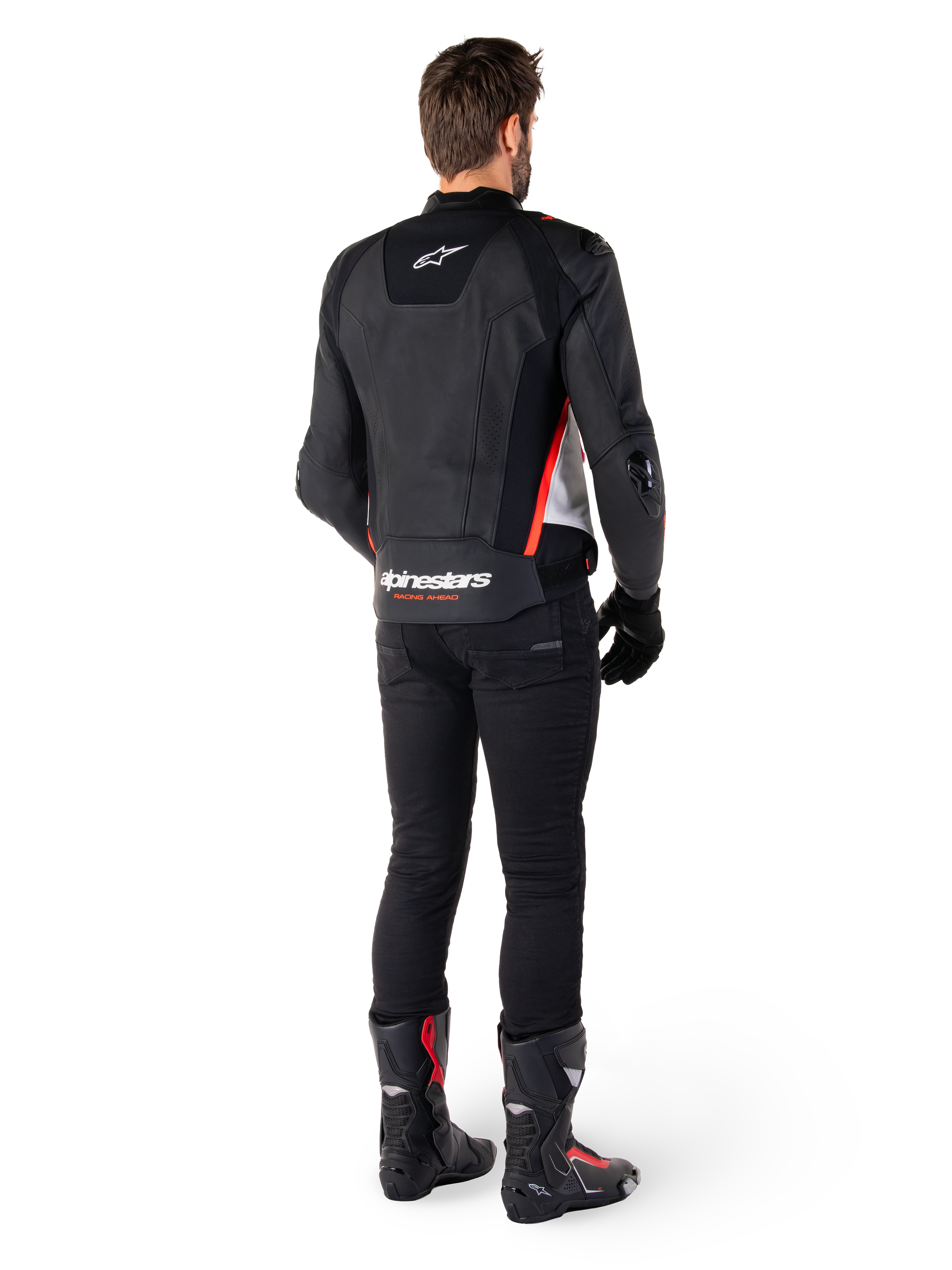 Alpinestars Missile V3 läderjacka i svart, vitt och röd fluo, vy bakifrån på en manlig förare, med Alpinestars-logotyper på övre och nedre ryggen, kombinerad med svarta byxor och motorcykelstövlar, racinginspirerad sportjacka i läder.