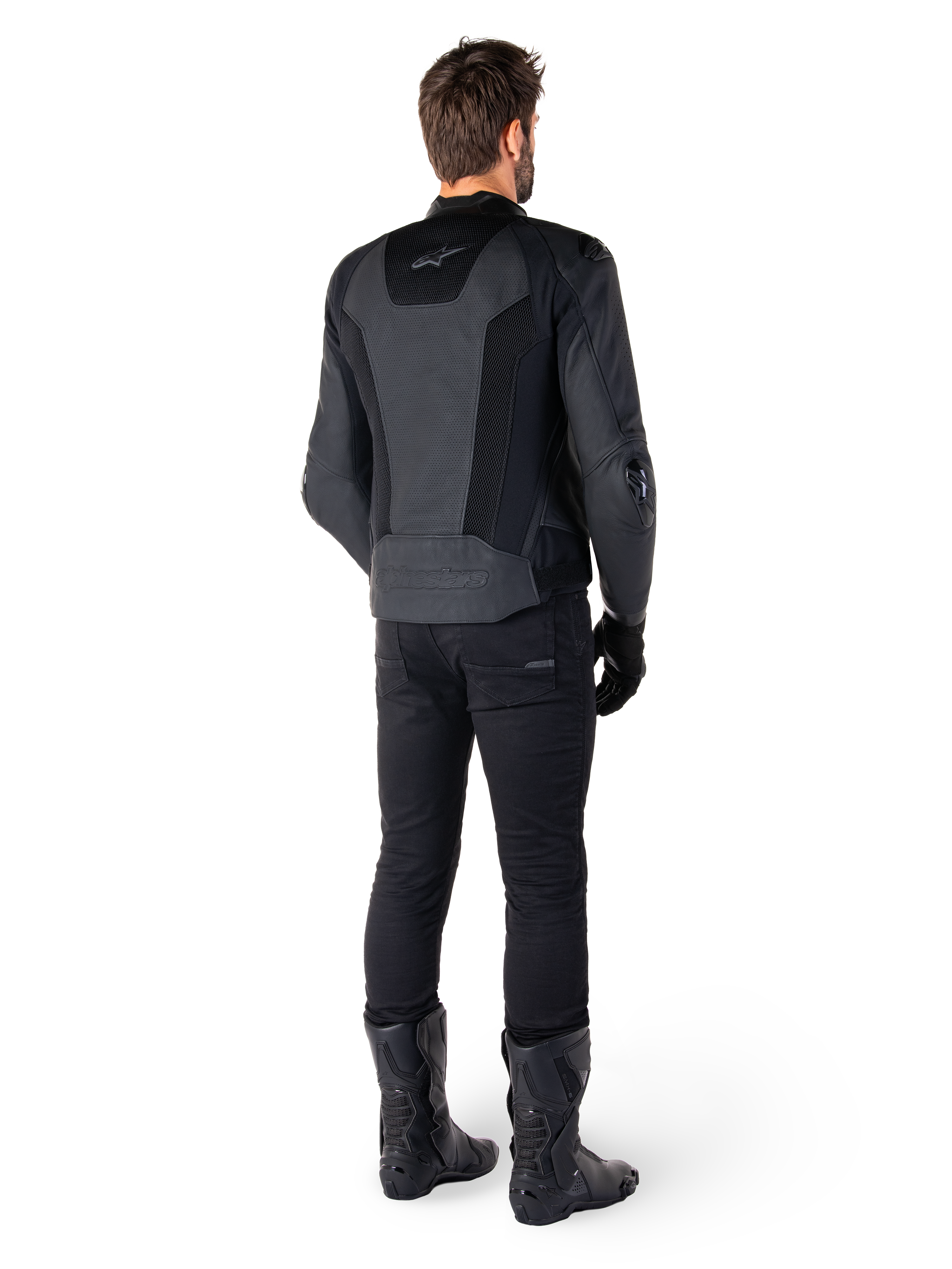 Bakifrån vy av en man klädd i Alpinestars Missile V3 Airflow skinnjacka i svart, med omfattande perforerade paneler för ventilation, matchad med svarta körbyxor och stövlar, vilket ger en strömlinjeformad racingestetik.