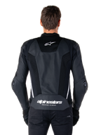 Alpinestars Missile V3 Airflow läderjacka, svart och vit, sedd bakifrån på en förare, med omfattande perforerade läderpaneler, vita sidodetaljer, Alpinestars stjärnlogotyp på den övre delen av ryggen och 'alpinestars RACING AHEAD'-logotyp på den nedre delen av ryggen.
