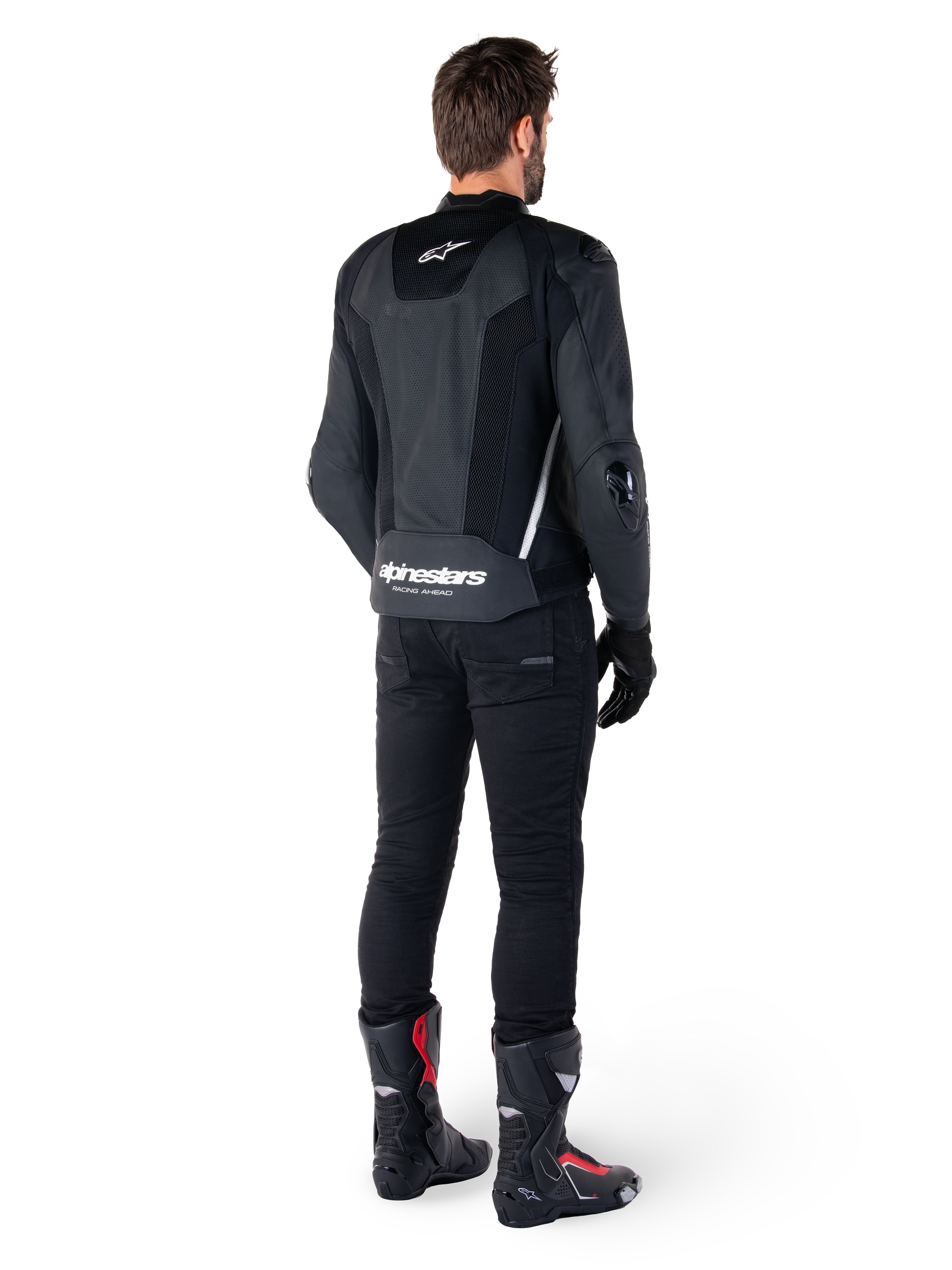Alpinestars Missile V3 Airflow skinnjacka, svart och vit, vy bakifrån buren med svarta tekniska byxor och racingstövlar, med perforerade läderpaneler på ryggen och tydlig Alpinestars-logotyp på nedre delen av ryggen.