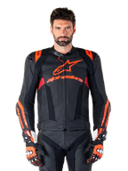 Alpinestars Missile V3 Ignition läderjacka, motorcykelracingjacka, svart och röd fluo, bärs med matchande racinghandskar och läderbyxor, med perforerad ventilation och framträdande Alpinestars-logotyper, professionell racingutrustning