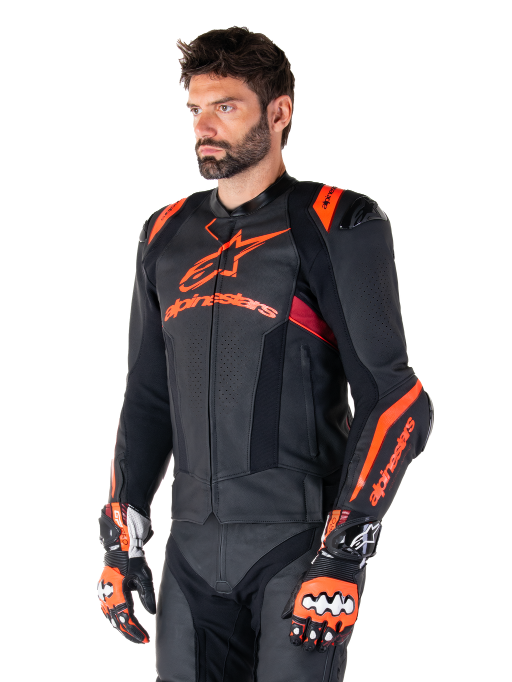 Alpinestars Missile V3 Ignition läderjacka, svart med Red Fluo- och mörkröda accenter, buren av en manlig modell med matchande racinghandskar och läderbyxor, med framträdande Alpinestars-logotyper, perforerade läderpaneler och externa axelskydd, professionell racingutrustning för motorcykel.