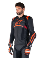 Alpinestars Missile V3 Ignition läderjacka, svart med Red Fluo- och mörkröda accenter, buren av en manlig modell med matchande racinghandskar och läderbyxor, med framträdande Alpinestars-logotyper, perforerade läderpaneler och externa axelskydd, professionell racingutrustning för motorcykel.