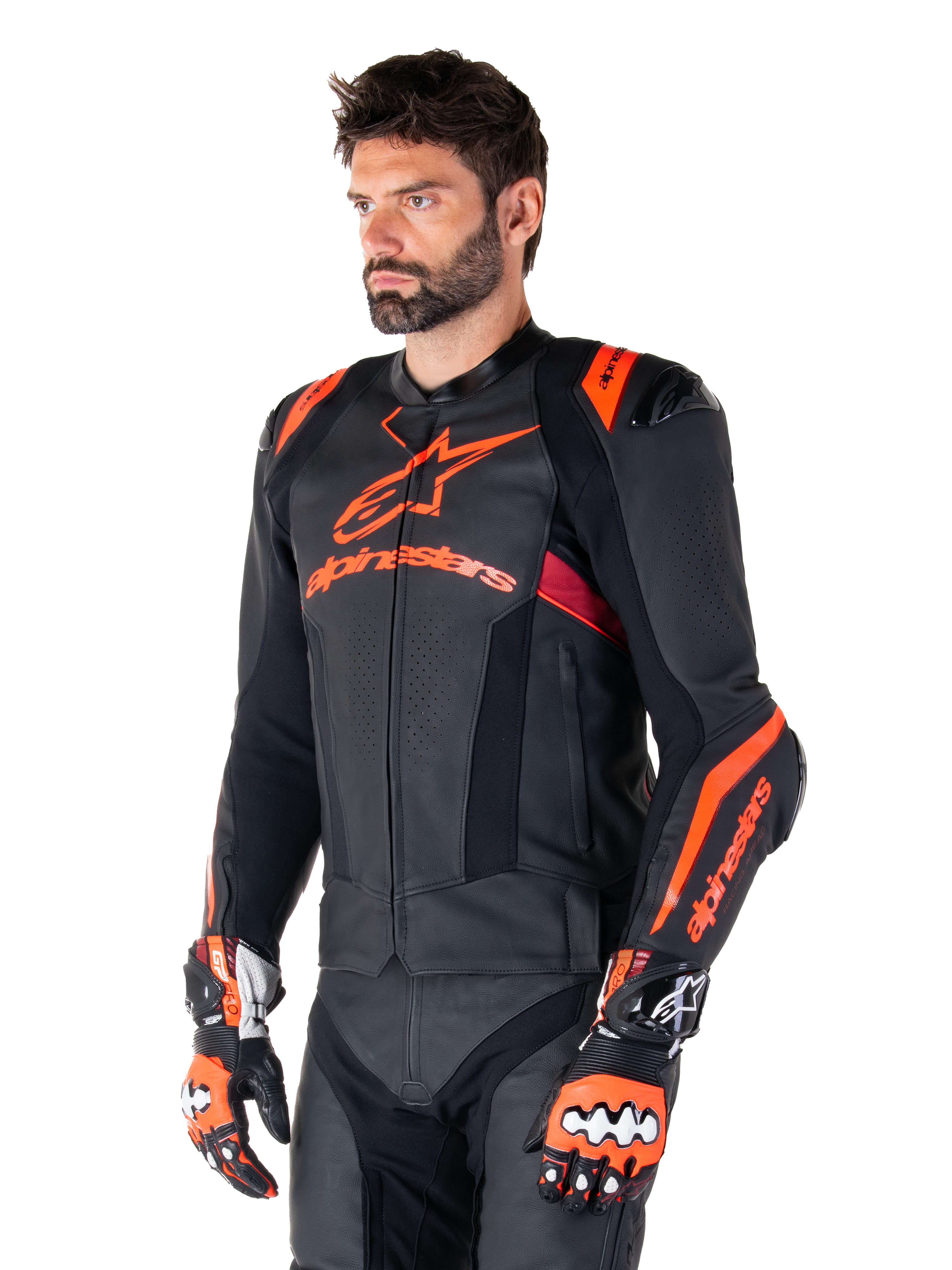 Alpinestars Missile V3 Ignition läderjacka, svart med Red Fluo- och mörkröda accenter, buren av en manlig modell med matchande racinghandskar och läderbyxor, med framträdande Alpinestars-logotyper, perforerade läderpaneler och externa axelskydd, professionell racingutrustning för motorcykel.