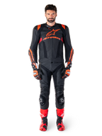 Manlig modell iklädd Alpinestars Missile V3 Ignition läderjacka i svart, röd fluo och mörkröd, komplett racingutrustning för motorcykel inklusive matchande läderbyxor, racinghandskar och stövlar, med framträdande Alpinestars-logotyp på bröstet, framåtvänd pose, professionell sportig MC-utrustning.