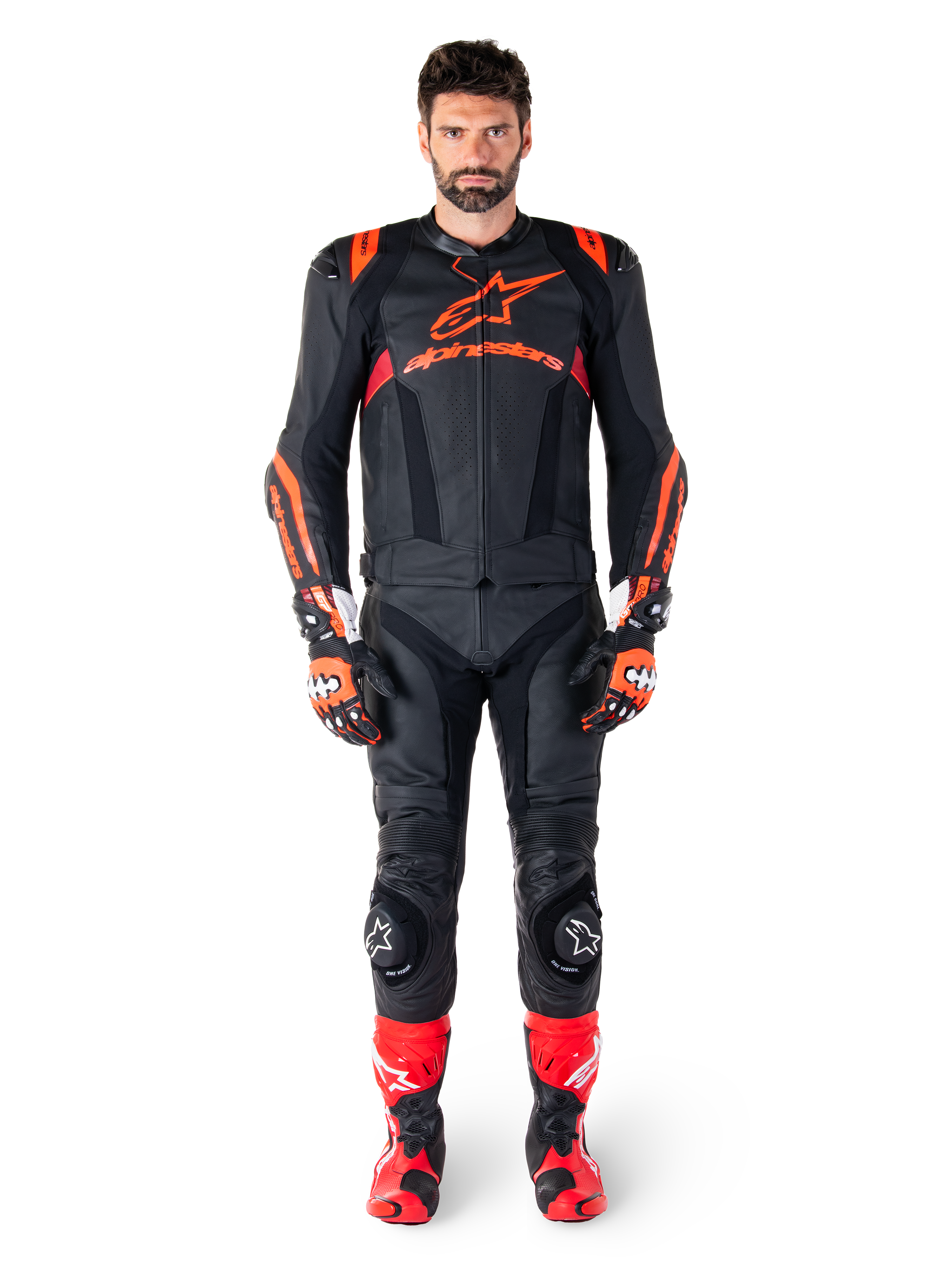 Manlig modell iklädd Alpinestars Missile V3 Ignition läderjacka i svart, röd fluo och mörkröd, komplett racingutrustning för motorcykel inklusive matchande läderbyxor, racinghandskar och stövlar, med framträdande Alpinestars-logotyp på bröstet, framåtvänd pose, professionell sportig MC-utrustning.