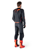 Alpinestars Missile V3 Ignition läderjacka, racingsportjacka för motorcykel, svart och röd fluo, bakifrån vy av en förare i ett komplett racingställ med matchande läderbyxor, handskar och röda stövlar, utrustad med sportig Aero-hump och tydlig logotyp på nedre ryggen.