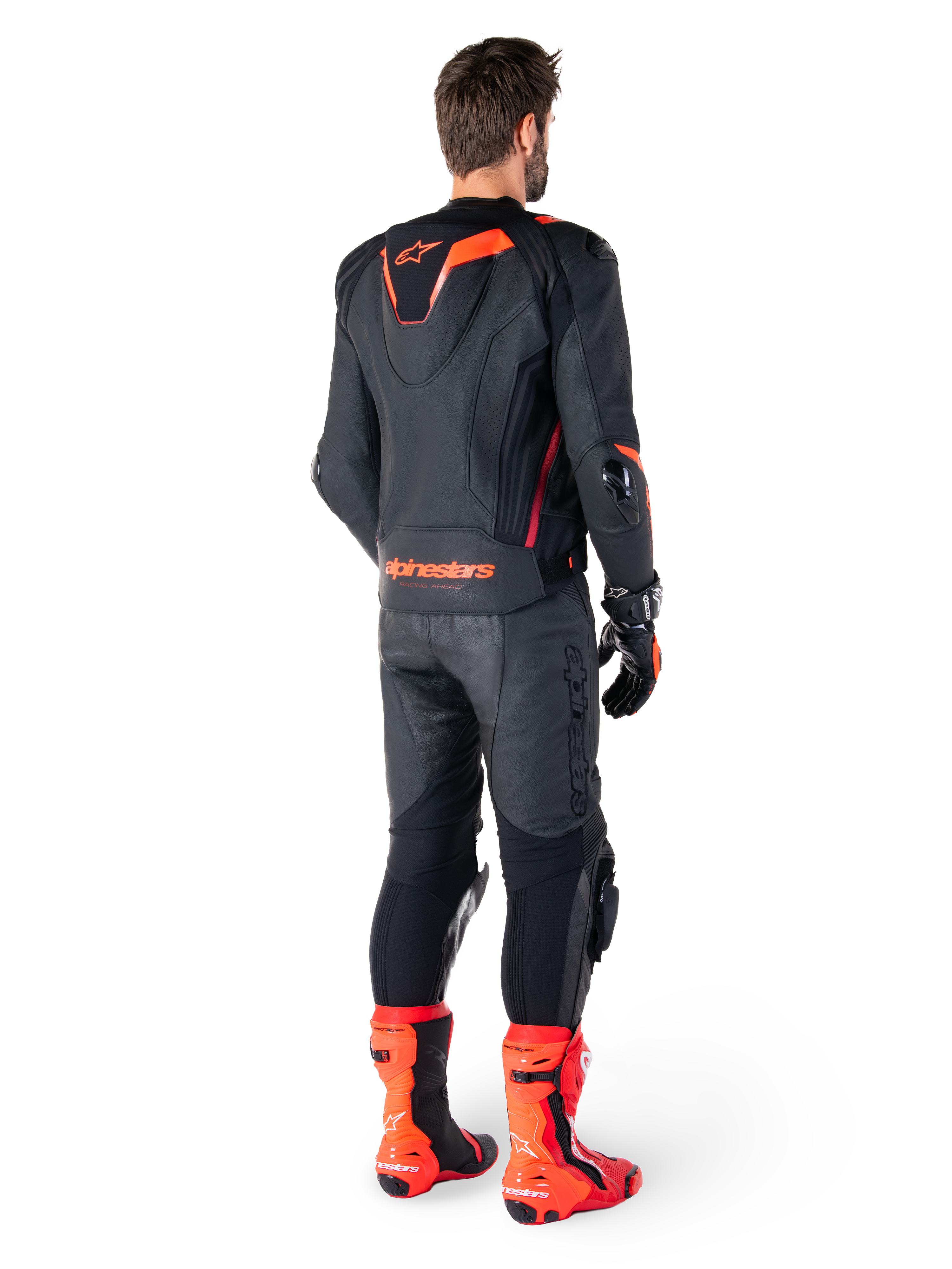 Alpinestars Missile V3 Ignition läderjacka, racingsportjacka för motorcykel, svart och röd fluo, bakifrån vy av en förare i ett komplett racingställ med matchande läderbyxor, handskar och röda stövlar, utrustad med sportig Aero-hump och tydlig logotyp på nedre ryggen.