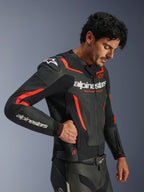 Alpinestars GP Force V2 Air Leather Jacket, Black and Red Fluo, perforated leather motorcycle jacket, model wearing the jacket and reaching into a zippered side pocket, featuring fluorescent red accents and white Alpinestars branding, professional sport riding gear.