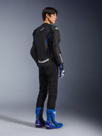 Modell sedd bakifrån bärande Alpinestars GP Force V2 Airflow läderjacka i Black Metallic Blue, med perforerade läderpaneler och vita logotyper, matchad med racinghandskar och blå stövlar, sportfokuserad MC-utrustning.