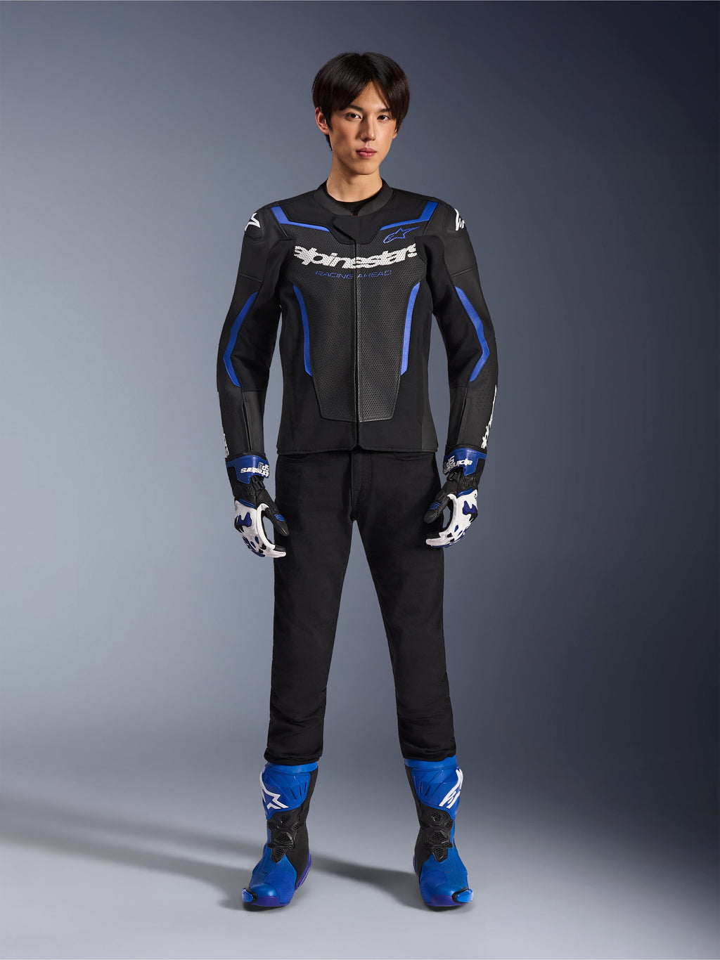 Alpinestars GP Force V2 Airflow läderjacka i Black Metallic Blue, matchande racinghandskar, svarta byxor och blå stövlar, professionell sportig motorcykelutrustning, helkroppsbild i studiomiljö