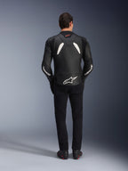 Model viewed from behind wearing the Alpinestars GP Plus V4 Leather Jacket in Black and White, paired with black pants and motorcycle boots, featuring white panels on the shoulders and Alpinestars logo branding on the sleeves and lower back.