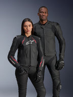 Alpinestars Stella Dusk läderjacka, Black Diva Pink White, bärs av en kvinnlig modell tillsammans med en manlig modell i matchande svart läderutrustning, med rosa och vita detaljer, vit stjärnlogotyp på bröstet och svarta mc-handskar