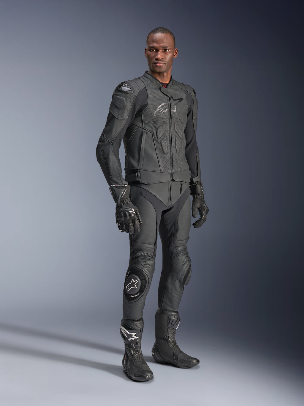 Alpinestars Dusk Airflow läderjacka, Black Black, bärs av en förare i komplett teknisk utrustning inklusive matchande läderbyxor, handskar och stövlar, med perforerade läderpaneler för ventilation och integrerade skydd för sportig motorcykelkörning.