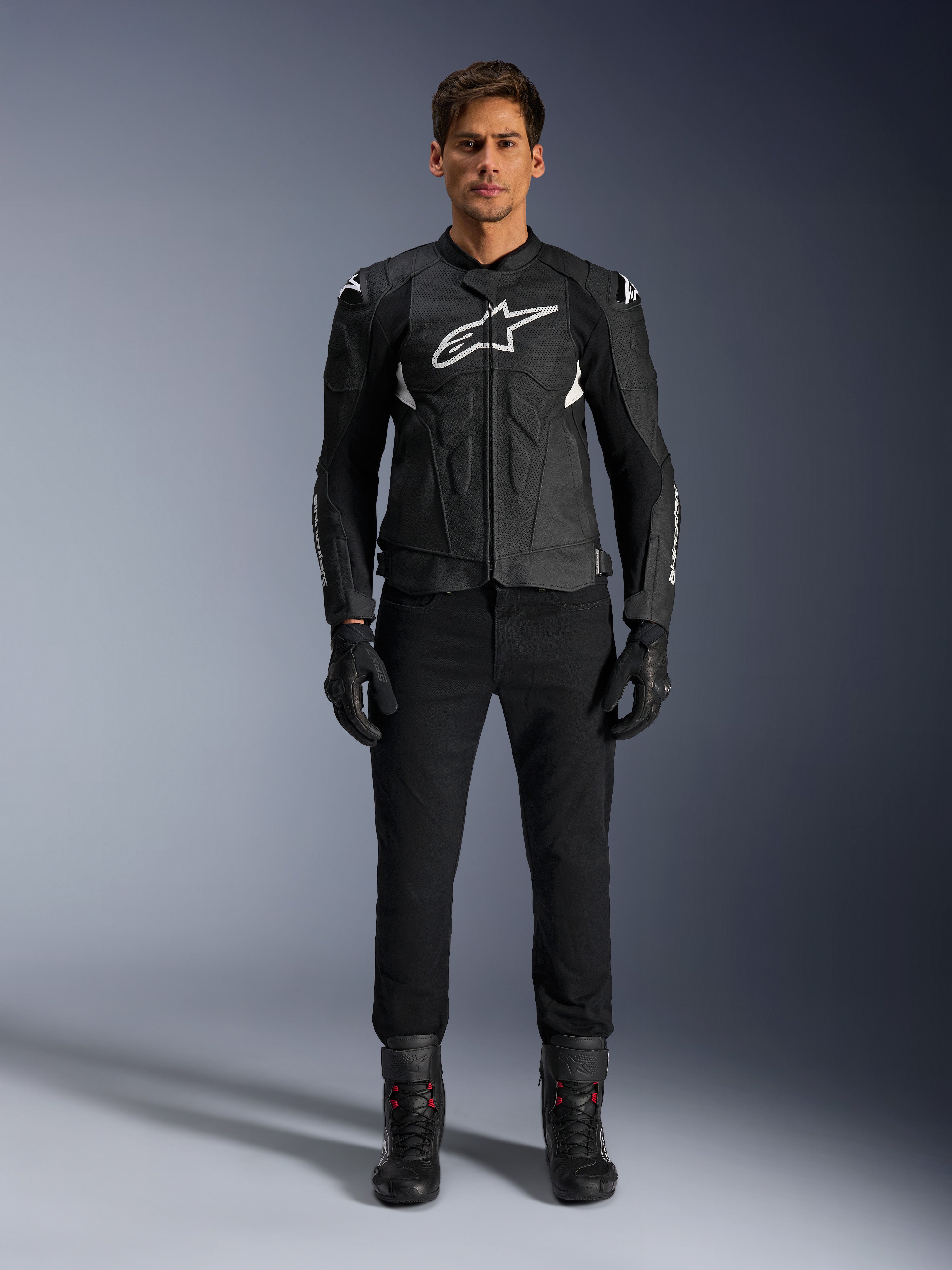 Alpinestars Dusk Airflow skinnjacka, svart och vit, motorcykeljacka i läder med perforerade paneler för luftflöde, vit Astars-logotyp på bröstet, bärs av en manlig förare med svarta byxor, handskar och mc-stövlar, professionell studiobild för sportmotorcykelutrustning.