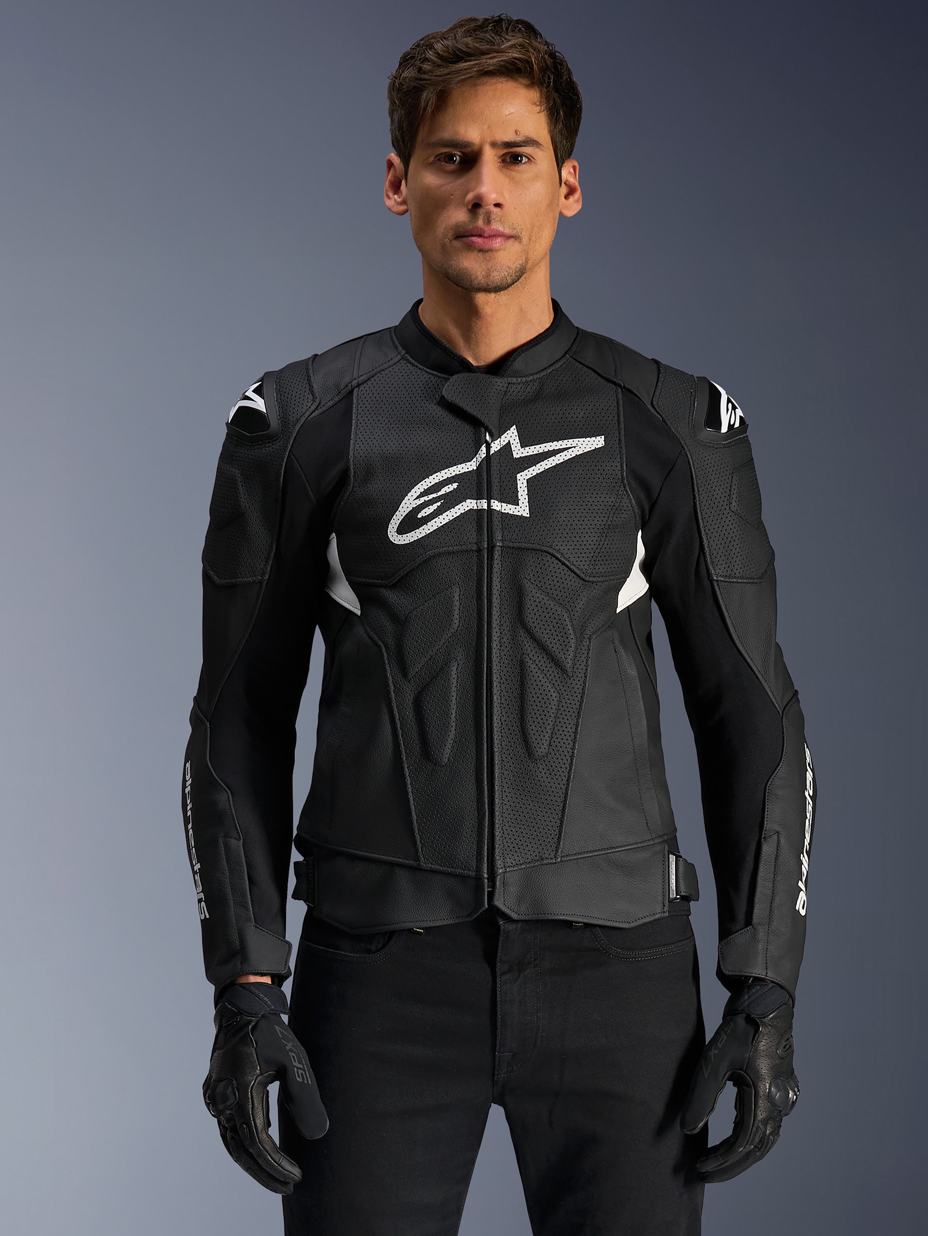 Alpinestars Dusk Airflow läderjacka, svart och vit, motorcykeljacka i läder som bärs av en modell, med perforerade läderpaneler för ventilation, en stor vit bröstlogotyp och externa axelskydd.