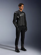 Alpinestars Dusk Airflow läderjacka, svart och vit, modellerad med svarta motorcykelbyxor, handskar och stövlar, med perforerade läderpaneler och vita logotyper, sportig road racing-stil.