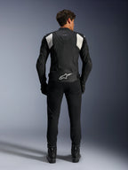 Alpinestars Dusk Airflow Läderjacka, svart och vit, vy bakifrån av en förare i svarta byxor och stövlar, med perforerat läder för ventilation, vita dragspelspaneler på axlarna och vit logotyp på nedre delen av ryggen