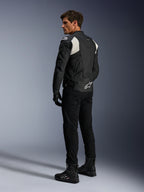 Alpinestars Dusk Airflow skinnjacka, svart och vit, vy bakifrån på modell som bär den perforerade skinnjackan med matchande svarta byxor och stövlar, vita dragspelsstretchpaneler och en tydlig logotyp på nedre delen av ryggen, sportig motorcykelutrustning