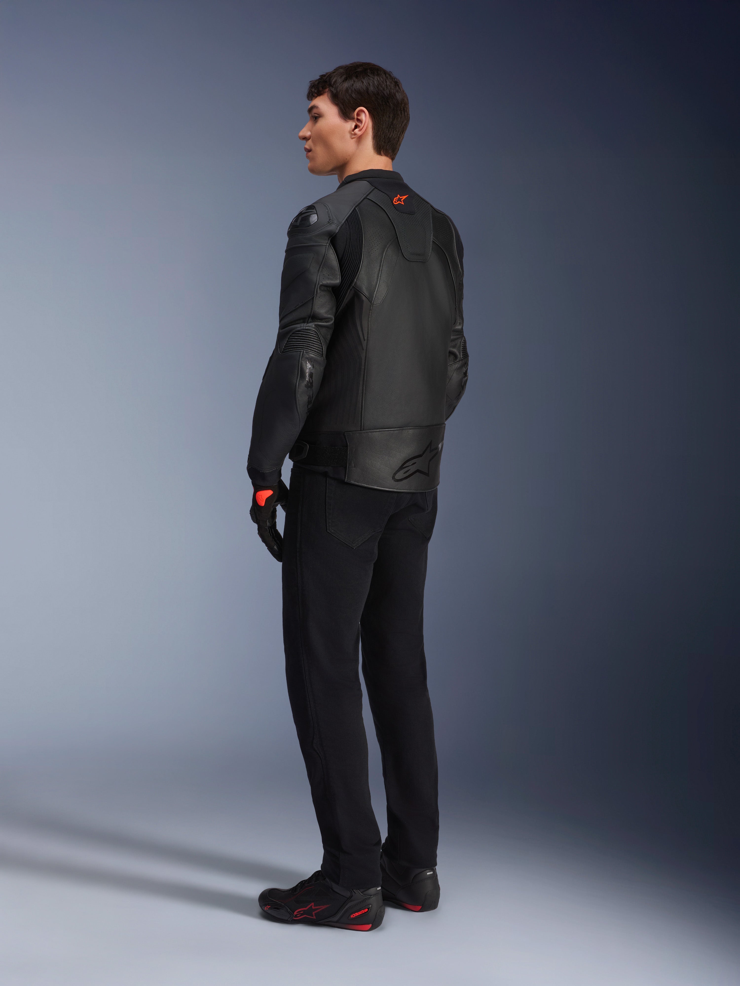 Alpinestars GP Plus R V4 Airflow Leather Jacket, Men's Sport Motorcycle Jacket, All Black, three-quarter rear view on a model, featuring perforated leather panels, red logo on the back, and integrated shoulder protection, worn with black pants and riding shoes