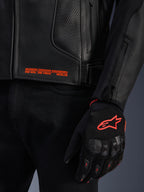 Alpinestars GP Plus R V4 Airflow Leather Jacket, close-up of black perforated leather with orange graphic text, paired with a black and orange motorcycle glove featuring the Astars logo