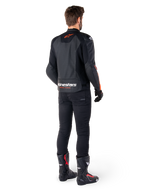 Alpinestars Faster V3 Airflow läderjacka, svart och röd fluo, sedd bakifrån på en förare, med perforerade läderpaneler och framträdande logotyper, bärs med svarta byxor och motorcykelstövlar, sportig mc-utrustning