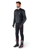 Man i Alpinestars Faster V3 Airflow läderjacka i Black Black, svarta byxor, svarta och röda motorcykelhandskar, svarta racingstövlar med röda och vita detaljer, komplett sportutrustning för motorcykelkörning