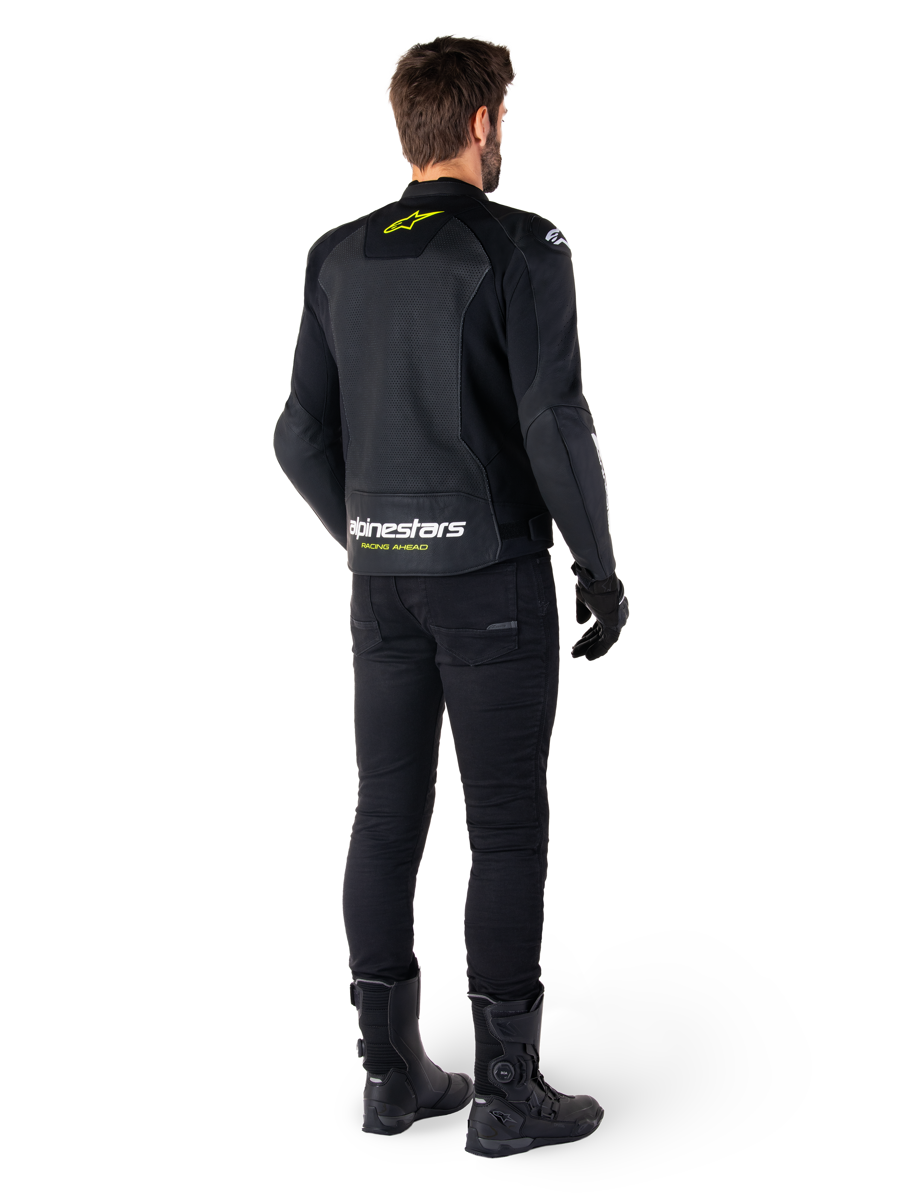 Rear view of a rider wearing the Alpinestars Faster V3 Airflow Leather Jacket, Black with White and Yellow Fluo accents, paired with black pants and boots, featuring perforated leather for ventilation and bold 'RACING AHEAD' branding on the lower back.