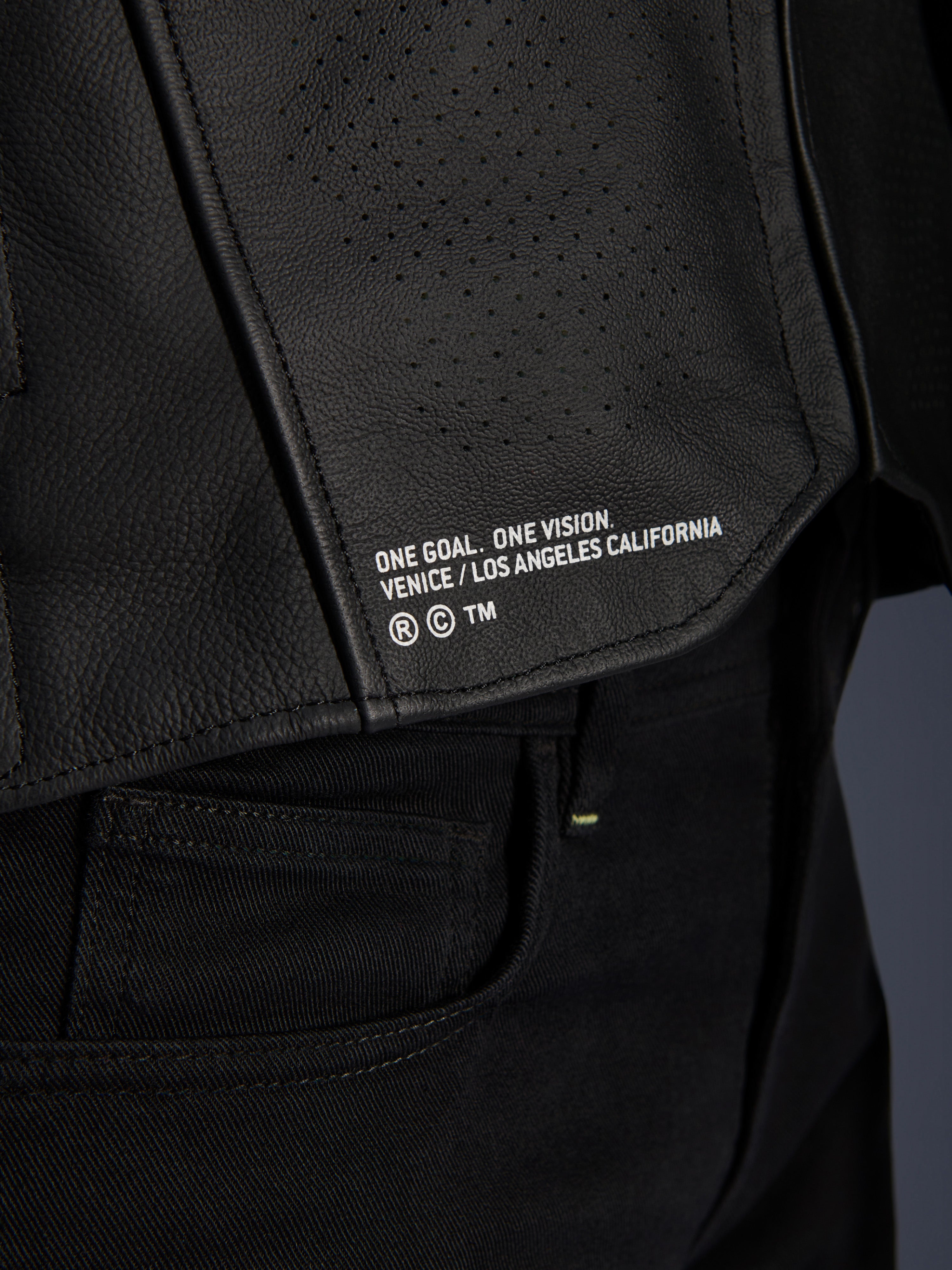 Närbild av Alpinestars Atem V5 läderjacka i svart, med den nedre ryggpanelen, 'ONE GOAL. ONE VISION. VENICE / LOS ANGELES CALIFORNIA'-tryck och perforerad läderstruktur.