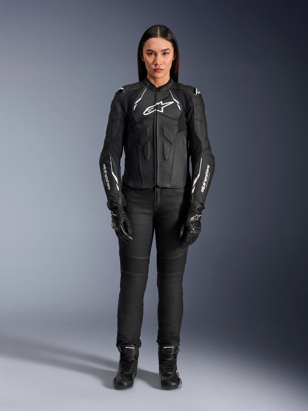 Alpinestars Stella Dusk läderjacka för dam, svart och vit, bärs av en modell med matchande svarta byxor och stövlar, vy framifrån, vita Alpinestars-logotyper på bröstet och ärmarna, skyddsutrustning i premium nötläder för damer