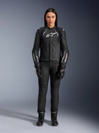Alpinestars Stella Dusk läderjacka för dam, svart och vit, bärs av en modell med matchande svarta byxor och stövlar, vy framifrån, vita Alpinestars-logotyper på bröstet och ärmarna, skyddsutrustning i premium nötläder för damer