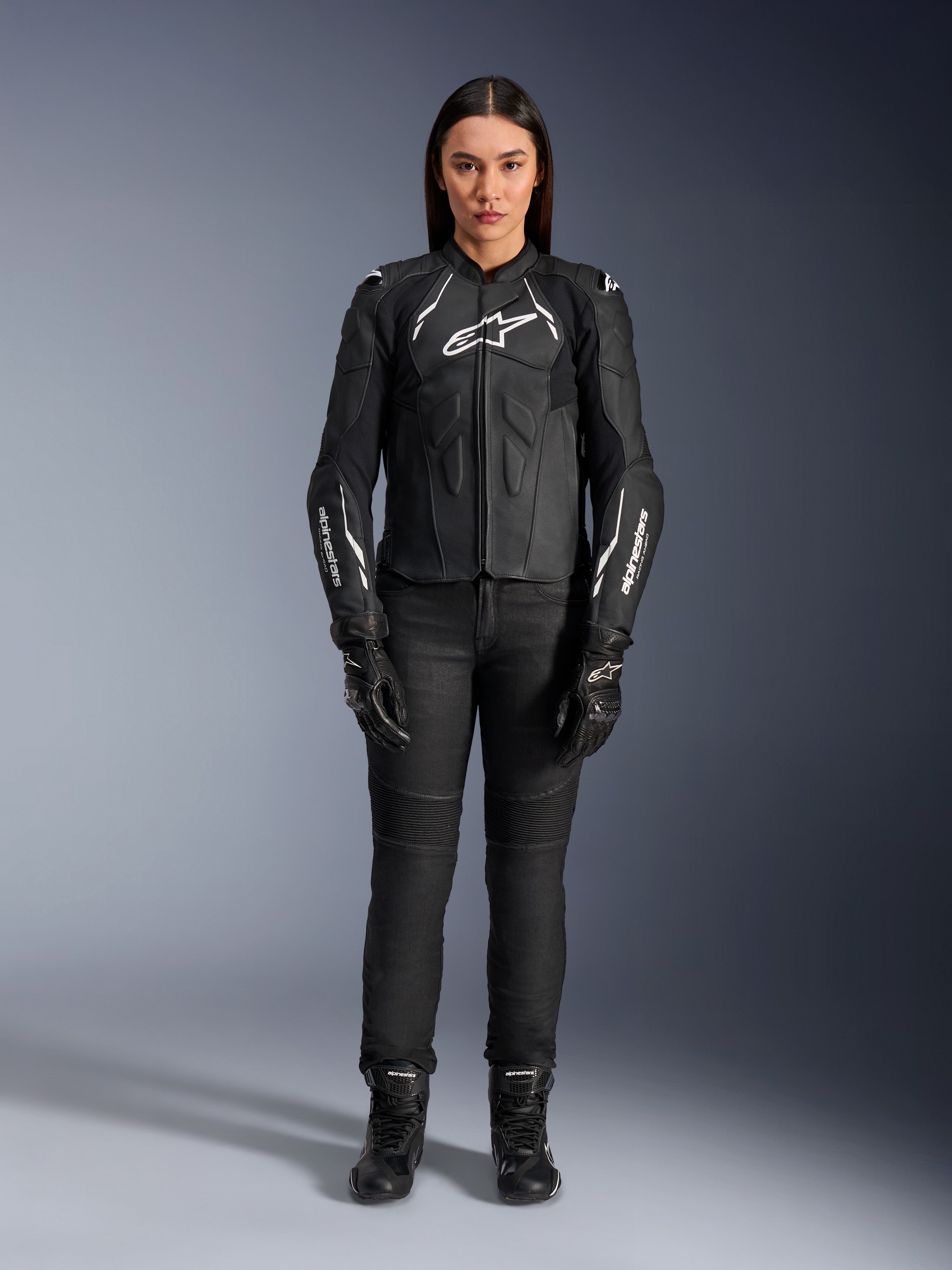 Alpinestars Stella Dusk läderjacka för dam, svart och vit, bärs av en modell med matchande svarta byxor och stövlar, vy framifrån, vita Alpinestars-logotyper på bröstet och ärmarna, skyddsutrustning i premium nötläder för damer