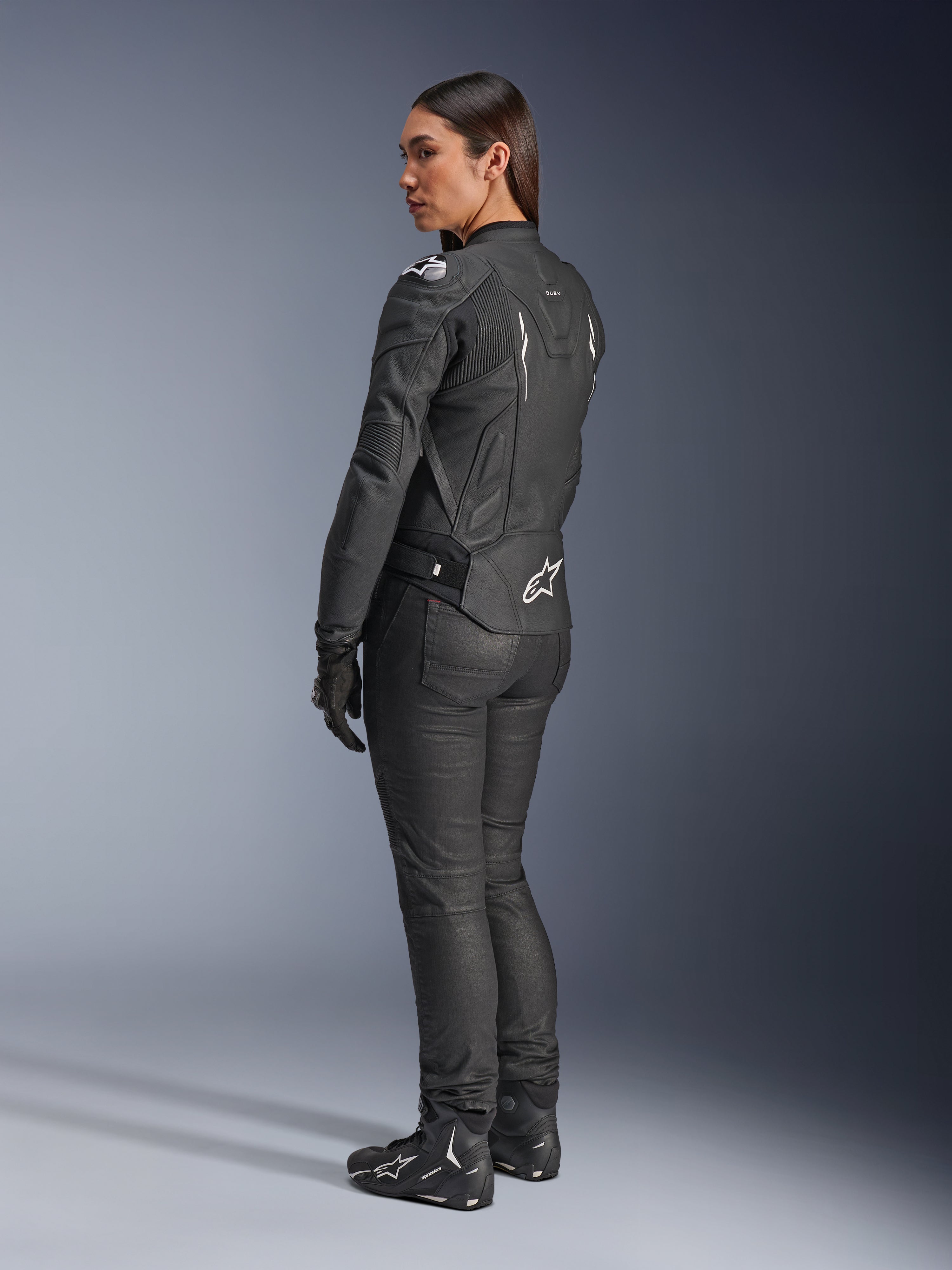 Alpinestars Stella Dusk läderjacka, motorcykeljacka för dam, svart och vit, vy bakifrån med vit Alpinestars-logotyp på ländryggen och axlarna, bärs med svarta mc-byxor och stövlar, sportfokuserad ergonomisk passform för vägkörning