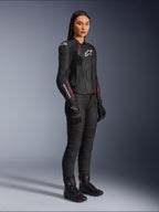 Alpinestars Stella Dusk skinnjacka för dam, svart, Diva Pink och vit, bärs av en kvinnlig modell med svarta motorcykelbyxor och stövlar, med en smidig läderkonstruktion, rosa detaljer och vita logotyper.
