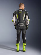 Alpinestars GP Tech V5 endelat skinnställ, vy bakifrån, svart, vit och neongul, med en aerodynamisk puckel med gul stjärnlogotyp, vita Alpinestars-logotyper på ärmar och rygg, matchande neongula racingstövlar, professionell motorcykelutrustning för bana.