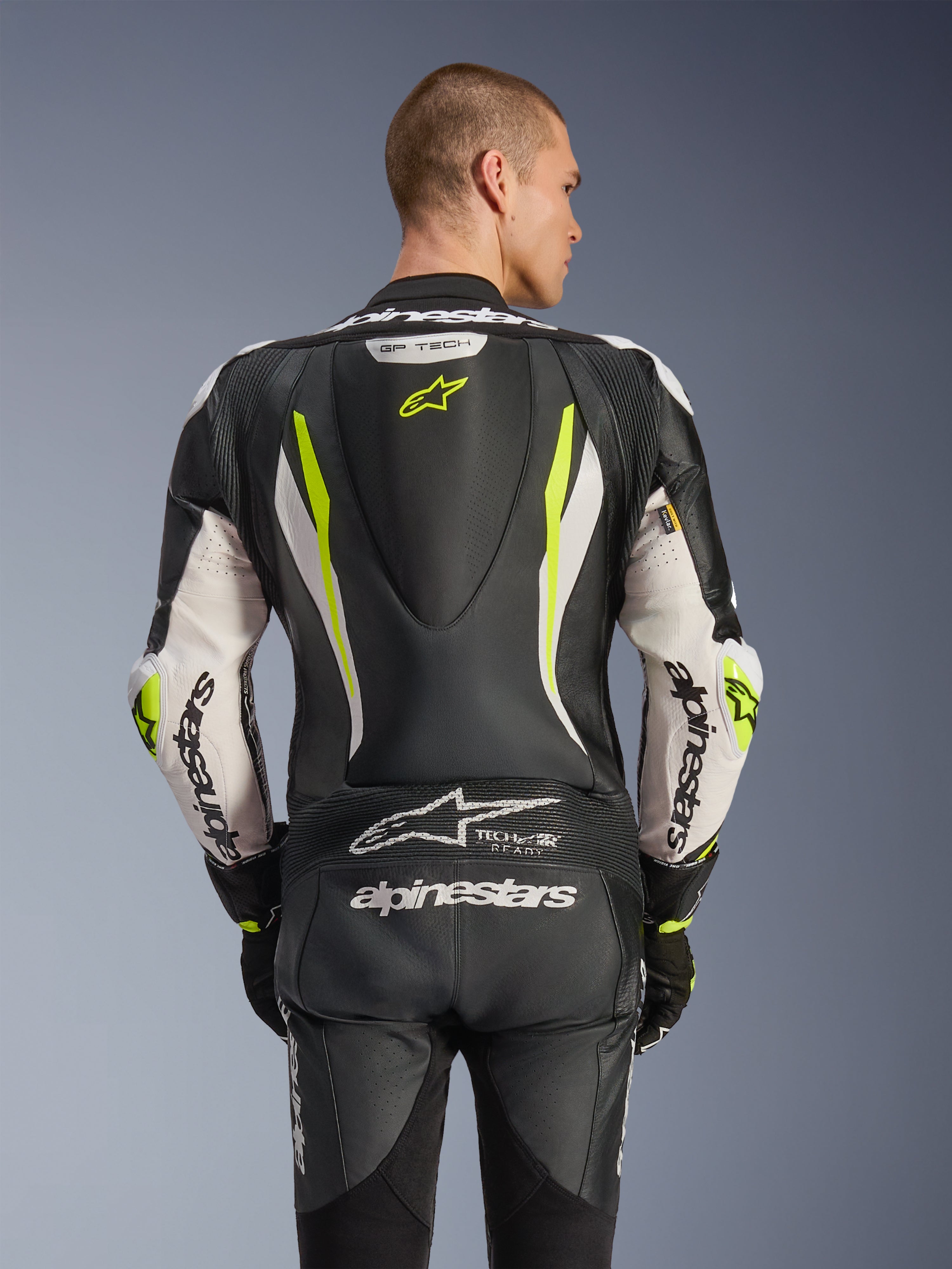 Alpinestars GP Tech V5 endels skinnställ, sedd bakifrån på modell, svart, vit och neongul, med aerodynamisk puckel, stor Alpinestars-logotyp på armar och sätet, dragspelspaneler i stretch och Tech-Air Ready-logotyp